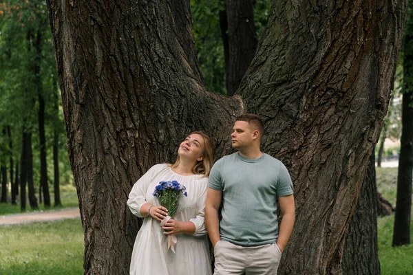 愛する夫婦の肖像画 男と公園の花を持つ妊婦は 幸せな家族が空を見る新しい追加を待っています — ストック写真