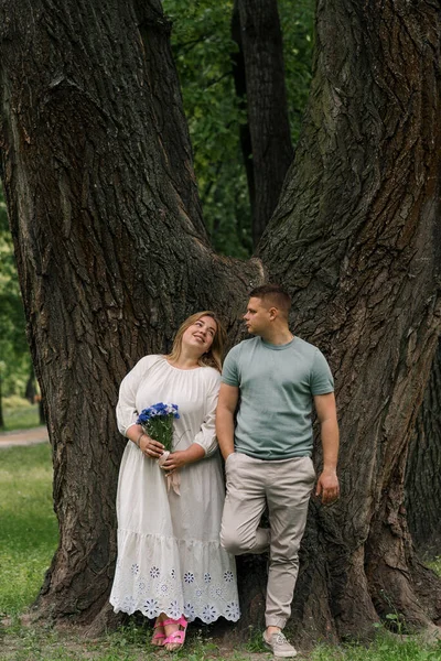 愛するカップルの肖像画 男と公園の花を持つ妊婦 カップルはお互いを見ている家族に新しい追加を待っています — ストック写真