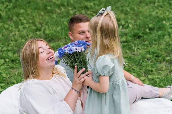 一个快乐的家庭在公园里的大自然中休息 一个穿着连衣裙的小女儿送给妈妈一束鲜花 — 图库照片