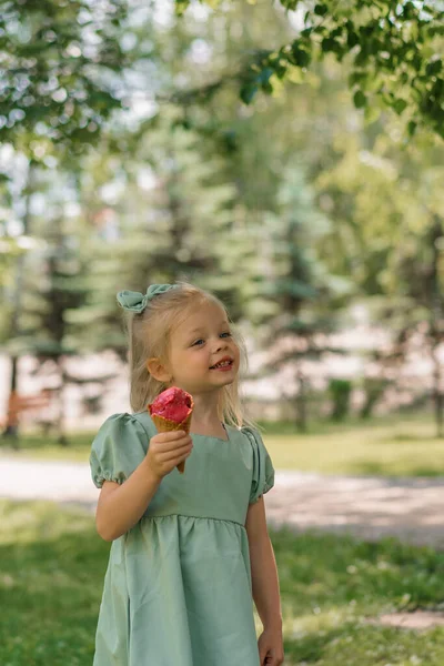 緑の夏のドレスの小さなかわいい女の子はアイスクリームの街公園夏の家族のライフスタイルの子供と美味しいアイスクリームの子供を食べる — ストック写真
