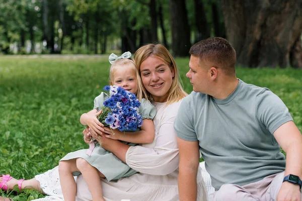公園の自然の中で幸せな家族は子供を抱きしめる小さな花の誕生日を祝います — ストック写真