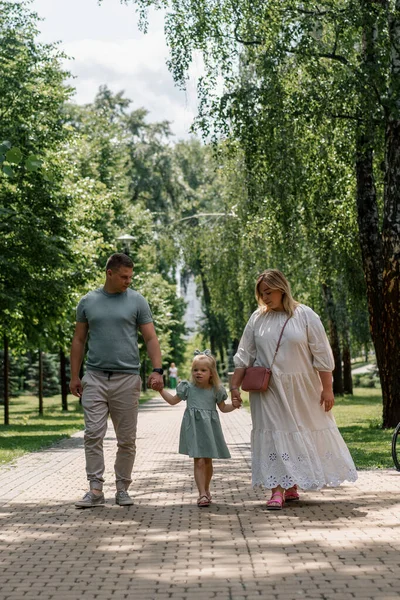穿着绿色夏装的可爱小女孩 和父母一起在城市公园里散步夏季家庭生活幸福的家庭牵着手 — 图库照片