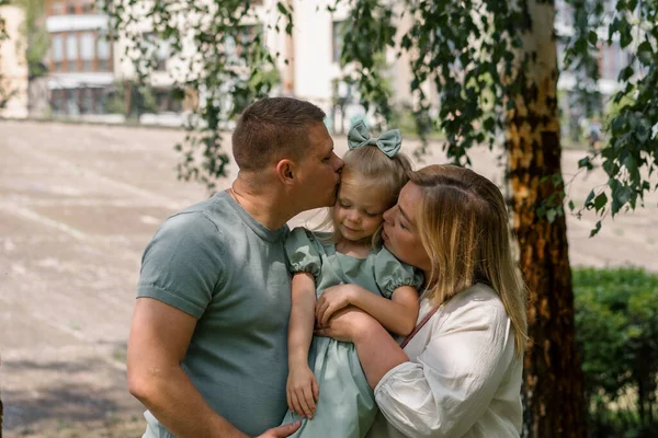 幸せな若い家族の母親と娘の両親の肖像画は 彼らの腕に赤ん坊の女の子を保持し 公園の子供時代の散歩で彼女の家族にキス — ストック写真