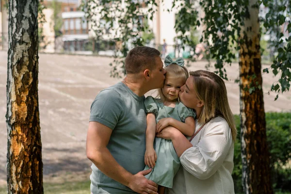 在公园里 父母抱着一个女婴 亲吻着她的家人散步 这是一个快乐的年轻家庭的画像 — 图库照片