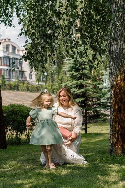 小女孩穿着绿色的夏装在公园里散步 和妈妈跳舞 牵着手 快乐地度过了家庭的夏天 — 图库照片