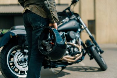 Yarış başlamadan önce elinde kaskla siyah bir motosikletin yanında duran vahşi motorcu. Hız tutkusu.
