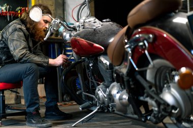 Yaratıcı otantik motosiklet atölyesi. Kızıl saçlı, sakallı, motorsikletli tamirci motorsikleti tamir etmeye odaklanıyor.