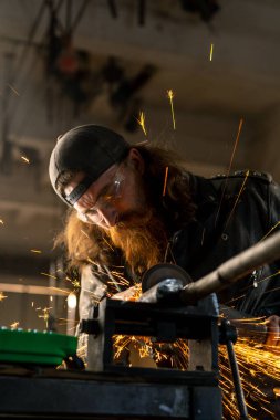Yaratıcı otantik motosiklet atölyesi kızıl sakallı vahşi motorcu sıcak metalden kıvılcımlar saçıyor.
