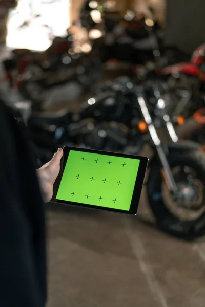 オートバイの近くに立って緑のスクリーンのタブレットを握るガレージの創造的な本物のオートバイの研修会のバイカーのメカニック — ストック写真