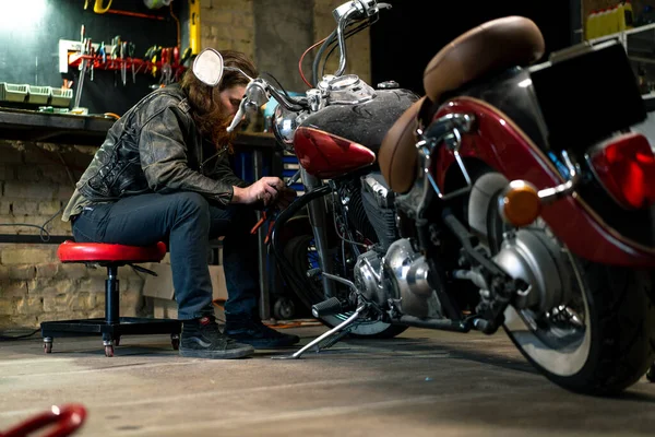 Creative authentic motorcycle workshop Garage redhead bearded biker mechanic is concentrating on repairing motorcycle