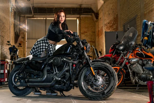 創造的な本物のオートバイの研修会のガレージクールなオートバイに座っている美しい若い少女バイカー — ストック写真