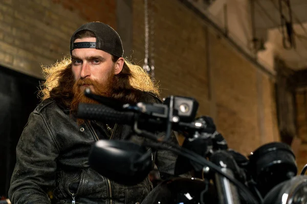 独创正宗的摩托车修车厂车库肖像画严肃的红头发 留着胡子的摩托车技师坐在摩托车上 — 图库照片