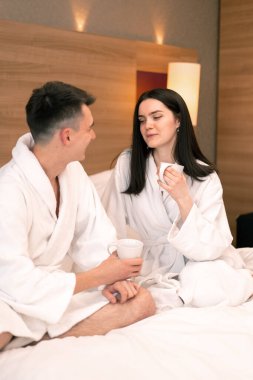 Genç çift balayında otel odasında kahvaltı yapıyor. Kahve içiyor, mutlu aşıklar seyahat ediyor.