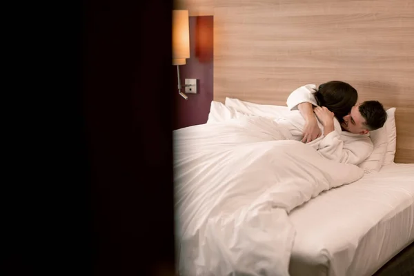 portrait young couple on honeymoon in hotel room lying on bed white robes kissing happy lovers travel concept