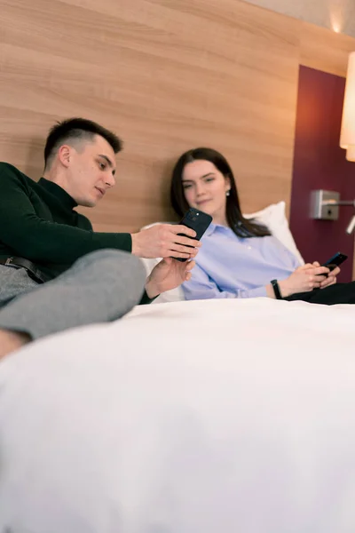 高級ホテルの部屋の部屋の若いカップル ベッドに横たわる恋人は 電話旅行コンセプトで面白いビデオを見ています — ストック写真
