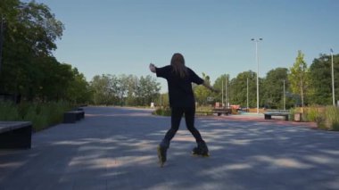 Sportif kız, şehir arka planında parkta paten sürüyor. Paten dersi sokak sporları konseptini seven aktif bir kız.