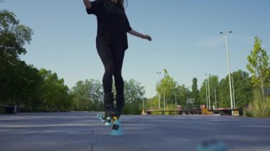 Parkın arka planında paten kayan sporcu kız sokak sporu konileri ile paten dersinin keyfini çıkarıyor.