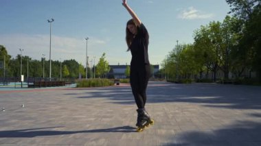 Sportif kız, şehir arka planında parkta paten sürüyor. Paten dersi sokak sporları konseptini seven aktif bir kız.
