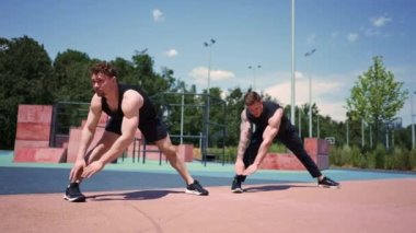 Kişisel fitness antrenörü spor sahasını eğitiyor. İki aktif adam dışarıda bacak egzersizi yapıyor.