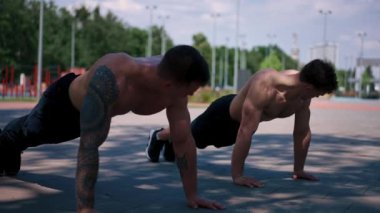 Genç sporcular antrenman sırasında sokaklarda şınav çekiyorlar. Kollar ve omuzlar seksi.