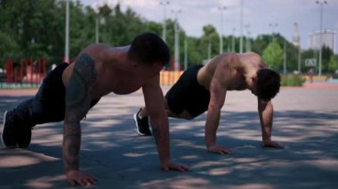 Genç sporcular antrenman sırasında sokaklarda şınav çekiyorlar. Kollar ve omuzlar seksi.