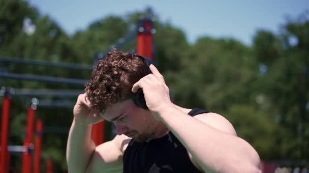 一名汗流浃背的年轻运动员在室外训练时在运动场用耳机听音乐的肖像 — 图库视频影像