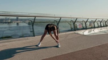Fitness genç sporcu kız sabah ısınma egzersizleri yapıyor. Şehirdeki köprüdeki spor salonunda antrenmandan önce.