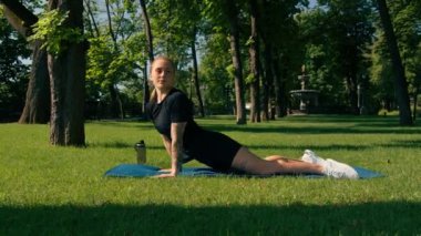 Genç sporcu kız spor minderi üzerinde fiziksel egzersiz yapıyor. Yoga eğitimi alıyor. Parkta çimenler üzerinde sağlıklı yaşam tarzı konsepti.