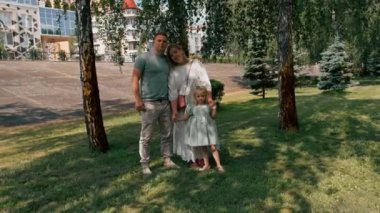Gülümseyen genç bir ailenin portresi. Anne, baba ve küçük kız aile parkta mutlu bir çocukluk geçiriyor.