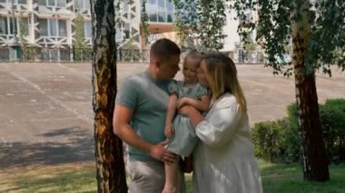 Gülümseyen genç bir ailenin portresi. Anne, baba ve küçük kız aile parkta mutlu bir çocukluk geçiriyor.