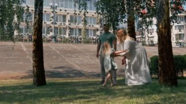 Yeşil elbiseli şirin bir kız. Ailesi şehir parkında yürüyor. Yazlık aile hayatı.
