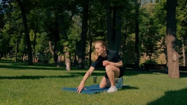 若いスポーツウーマンガールは 公園の外でトレーニングする前に手で水のカラマとボトルを保持し 草の健康的なライフスタイルのコンセプトにマットを置きます — ストック動画
