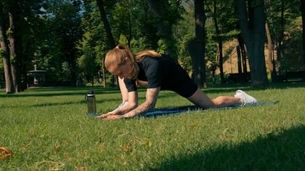 年轻的女运动员在公园外面做运动垫上的运动瑜伽训练 内容是草的健康生活方式的概念 — 图库视频影像