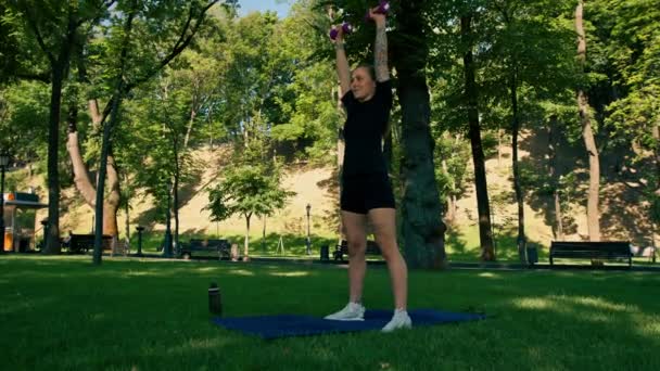 在公园健康生活理念的运动中 一个年轻的 心满意足的女运动员在室外用哑铃做运动的肖像 — 图库视频影像
