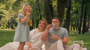 Mutlu aile parkta dinleniyor baba ve kız sabun köpüğü üflüyor eğlenceli çocukluk ailesi hafta sonu eğlencesi