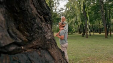 Neşeli küçük çocuk babasının yanında geziyor. Neşeli çocuk babasının omuzlarında oturuyor. Babalar gününde mutlu bir aile yürüyüşü.