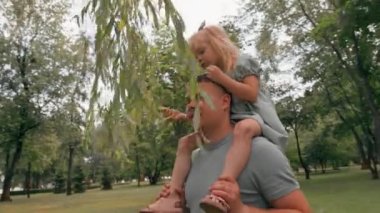 Neşeli küçük çocuk babasının yanında geziyor. Neşeli çocuk babasının omuzlarında oturuyor. Babalar gününde mutlu bir aile yürüyüşü.