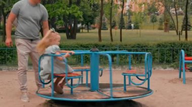 Yeşil yazlık elbiseli şirin bir kız çocuk parkında başını eğmiş babası atlıkarınca kızına biniyor yaz çocukluğunda