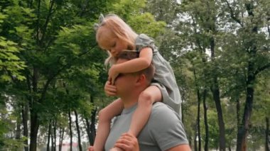 Neşeli küçük çocuk babasının yanında geziyor. Neşeli çocuk babasının omuzlarında oturuyor. Babalar gününde mutlu bir aile yürüyüşü.