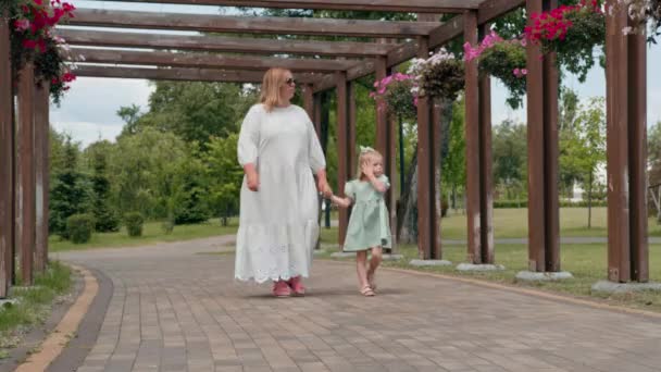 在公园里 一个身穿绿色夏装 头戴蝴蝶结的可爱小女孩在与怀孕的妈妈散步时度过了童年的暑假 — 图库视频影像