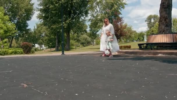 緑の夏のドレスの小さなかわいい女の子は 公園の子供時代の夏の家族休暇の母親の日に妊娠した母親と散歩で弓で — ストック動画
