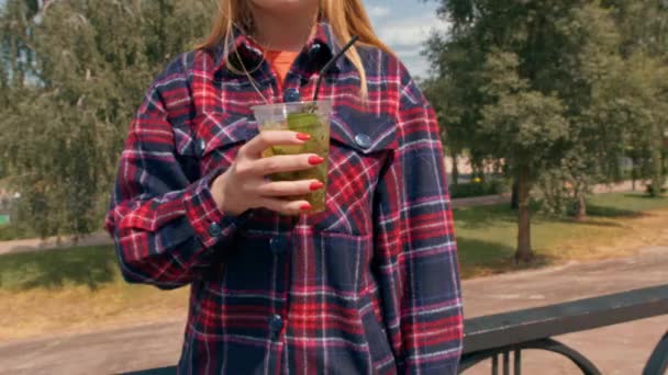夏に街を歩く若い女の子は 通りで冷たいおいしいカクテルを飲み カメラにカクテルを示しています — ストック動画