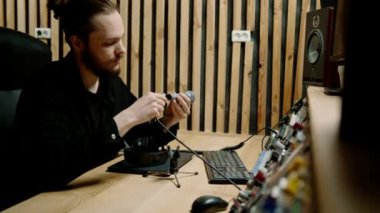 ses mühendisi mikrofonu profesyonel kayıt stüdyosundaki müzik ekipmanlarına bağlıyor.
