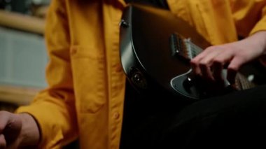 Kayıt stüdyosunda elektro gitarlı bir rock sanatçısı, telle bağlanan bir müzik aletini elinde tutuyor.