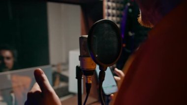 Genç pop rap sanatçısı, cam arkasında profesyonel kayıt stüdyosunda yeni bir şarkı kaydediyor.