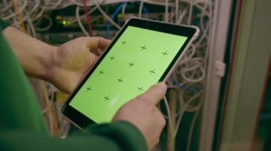 Veri Merkezi 'nin yakın plan hackerı ya da mühendisi elinde yeşil ekran tableti olan el sunuculardan bilgi çalıyor.