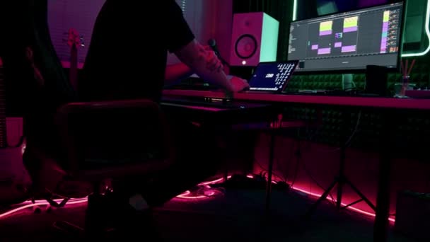 スクリーンネオンライトのリモコンミキシングトラックに座っているプロのサウンドレコーディングスタジオサウンドエンジニアまたは音楽プロデューサー — ストック動画