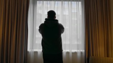 Otel odasındaki perdeleri pencere manzaralı iş merkezi seyahat konseptiyle açan adam.