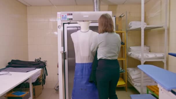 ハウスキーピング労働者は洗濯室の産業ホテルのホスピタリティの概念のアイロン掛けの衣服のためのマネキンにジャケットを置きます — ストック動画