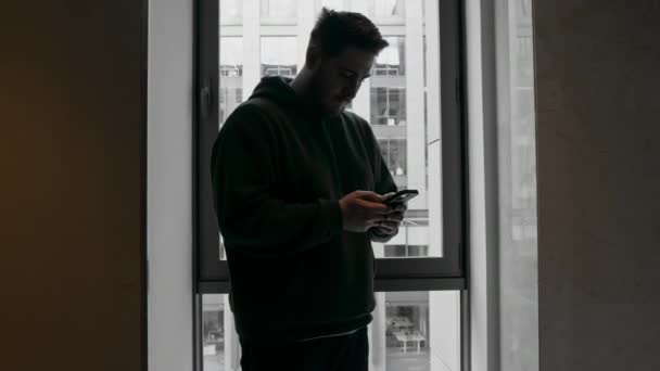 携帯電話を持った男は ビジネスセンターの視点で窓の背景にあるビジネス上の問題を解決します — ストック動画